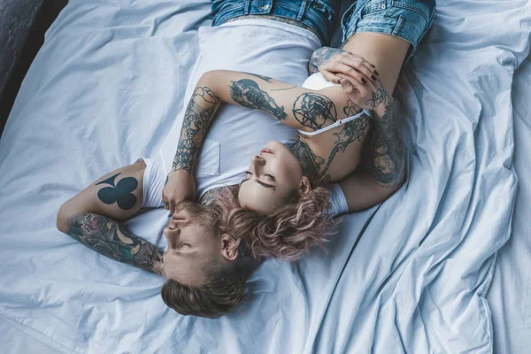 top view of tattooed couple hugging and resting on bed