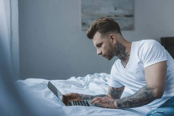 Yakışıklı Rahat Dövmeli Adam Yatakta Dizüstü Bilgisayar Kullanarak — Stok fotoğraf