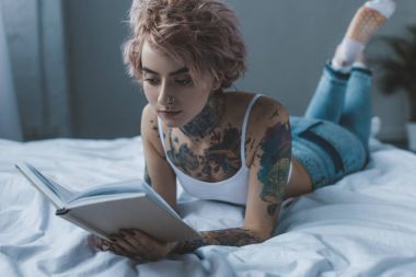 genç kız yatakta yatarken kitap okuma pembe saçlı dövme 