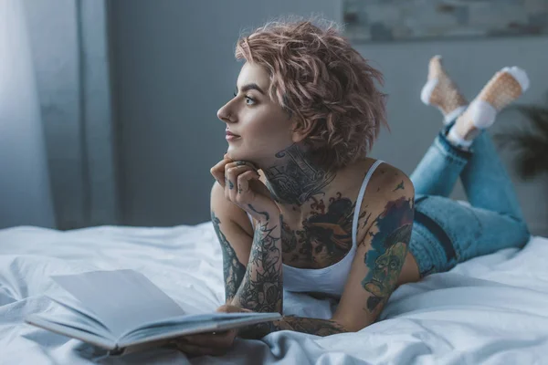 Задумчивая Татуированная Девушка Лежит Кровати Книгой — стоковое фото
