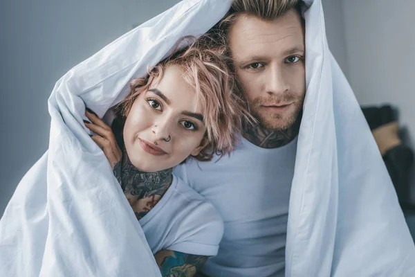 Young Tattooed Couple Looking Camera White Blanket Bedroom — Stock Photo, Image