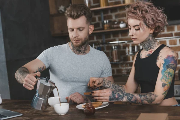 tattooed couple eating toasts and drinking coffee for breakfast