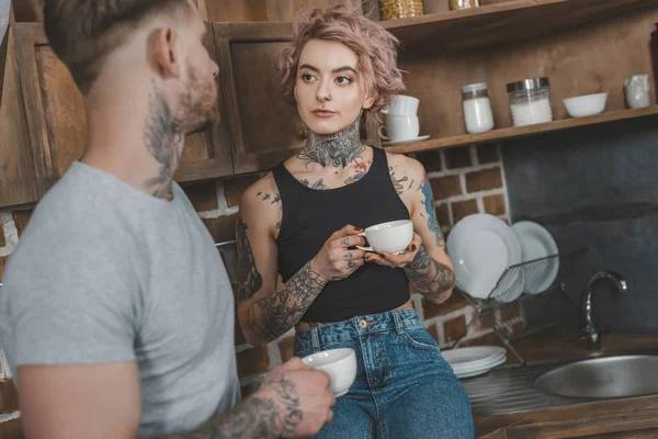 young tattooed couple drinking coffee together at morning