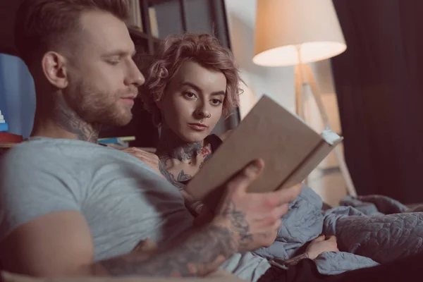 Pareja Tatuada Leyendo Libro Mientras Está Acostado Sofá Casa —  Fotos de Stock