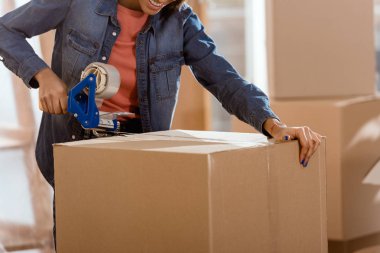 cropped view of african american woman packing cardboard box with scotch tape clipart