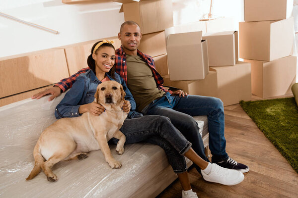 african american couple with labrador dog resting on sofa in new home