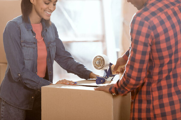 happy african american couple packing cardboard box to move in new home
