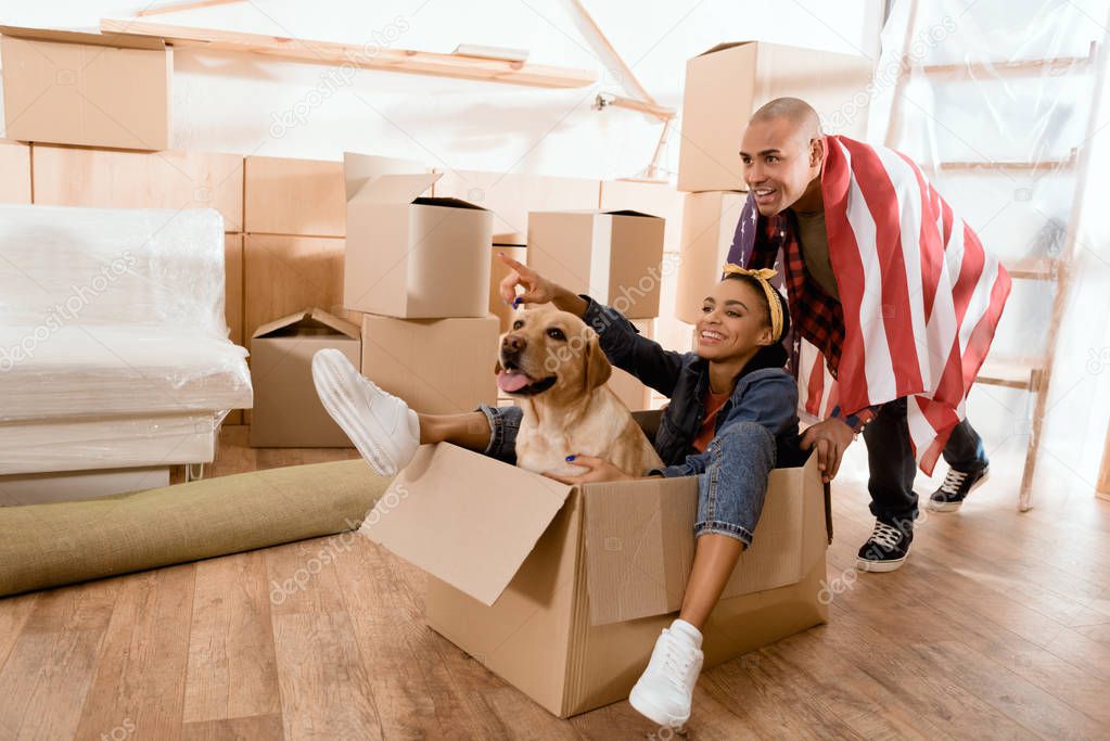 african american couple having fun with dog in new apartment