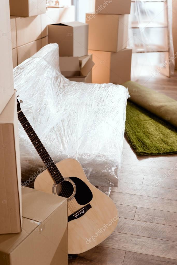 sofa, acoustic guitar, rolled carpet and cardboard boxes in new home