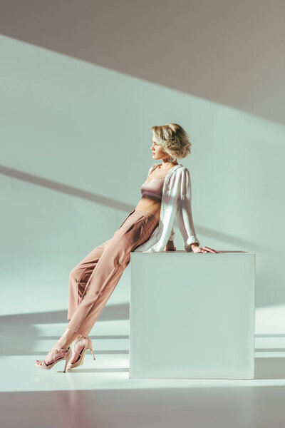beautiful charming blonde woman in pink bra, shirt and pants sitting and looking away in studio   