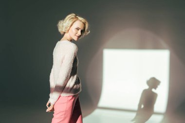 beautiful blonde girl smiling at camera while posing in studio clipart