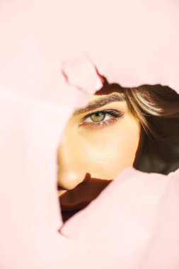 güzel kız kamera yırtık pembe kağıt üzerinden bakarak   