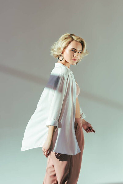 beautiful blonde woman in pink bra, shirt and pants looking at camera on grey