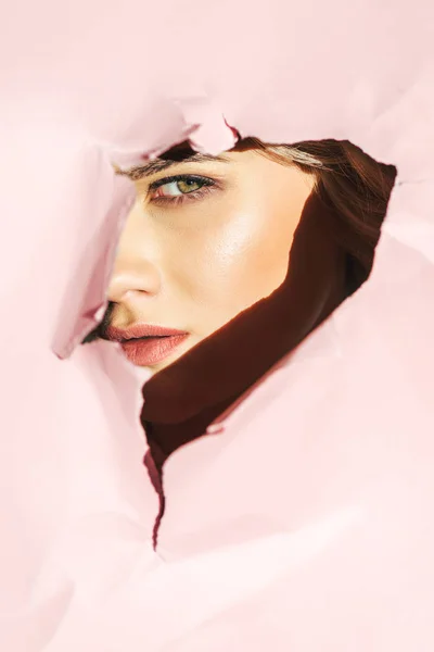 Привлекательная Молодая Женщина Смотрит Камеру Сквозь Рваную Розовую Бумагу — стоковое фото