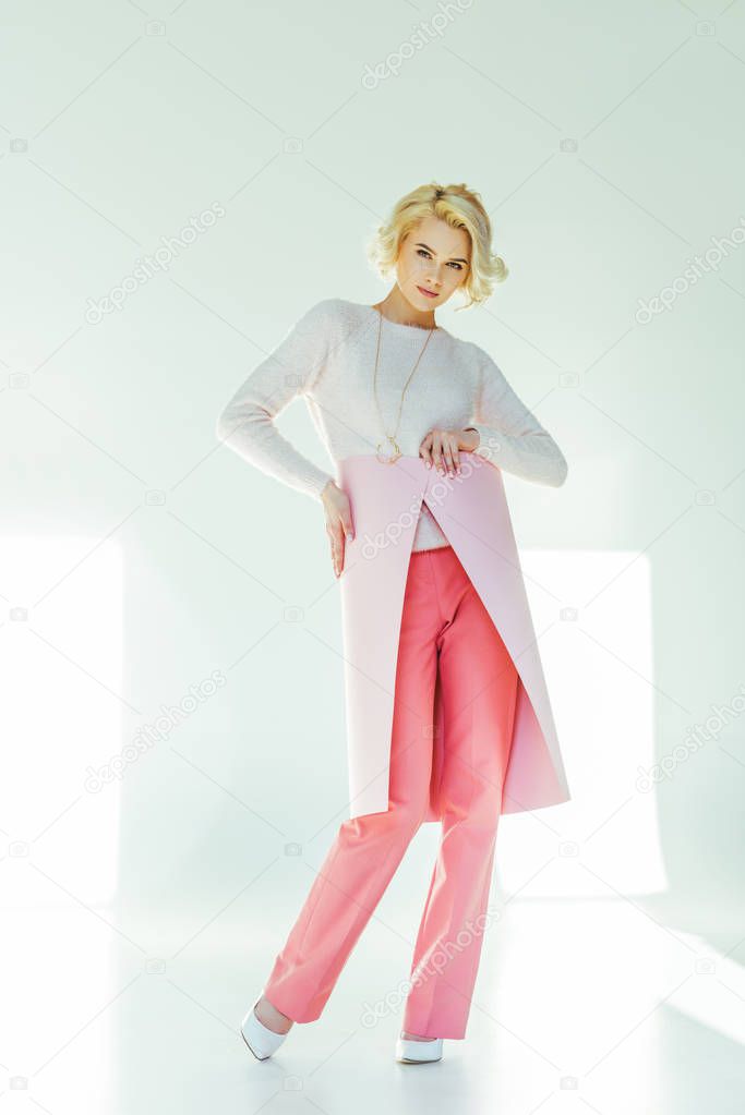 beautiful stylish blonde woman posing with pink banner and looking at camera on grey 