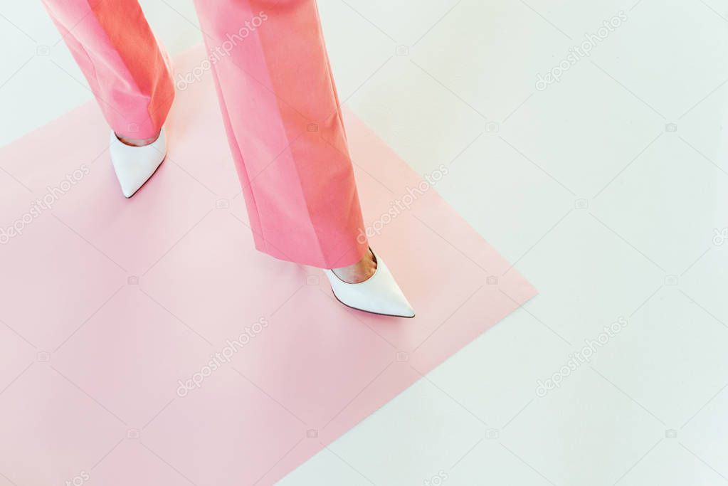 cropped shot of girl in pink pants standing on pink paper on grey