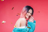happy beautiful girl posing in blue fur coat, isolated on pink with confetti