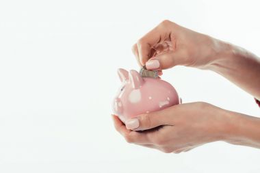 cropped view of woman putting coin into little piggy bank, isolated on white
