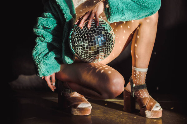 cropped view of stylish girl in green fur coat holding disco ball