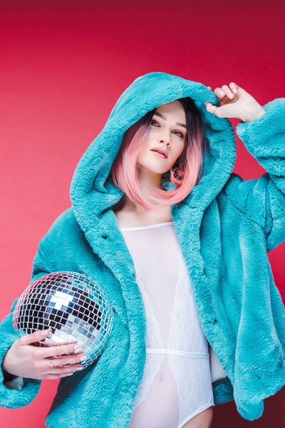 fashionable girl posing in blue fur coat with disco ball, isolated on pink