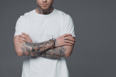 cropped shot of young man with tattoos standing with crossed arms isolated on grey clipart