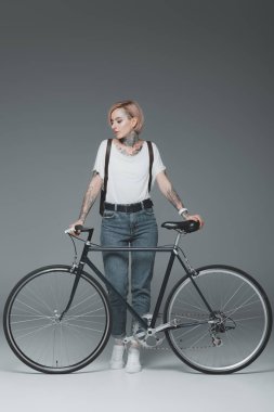 beautiful stylish girl with tattoos standing with bicycle isolated on grey clipart