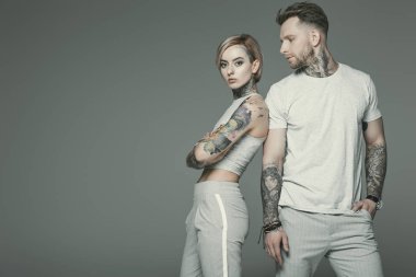 stylish tattooed couple in sportswear posing together, isolated on grey   clipart