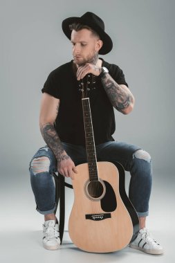 gri izole akustik gitar ile siyah şapkalı şık dövmeli gitarist