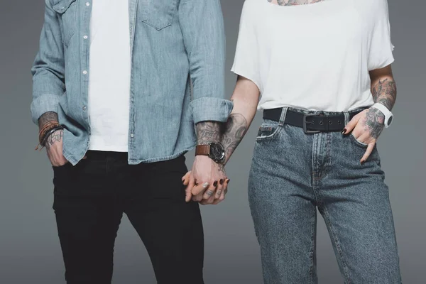时尚的年轻纹身夫妇手牵着手在灰色 — 图库照片