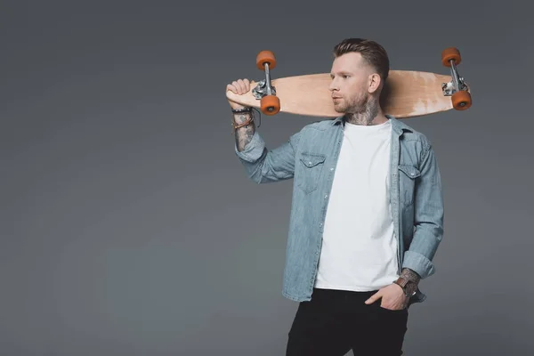 Pohledný Mladý Muž Tetováním Držení Skateboardu Koukal Izolované Grey — Stock fotografie