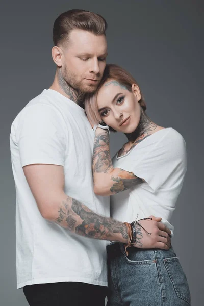 beautiful stylish young tattooed couple in white t-shirts hugging isolated on grey