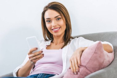 Smartphone kullanarak ve koltukta oturan neşeli güzel kadın