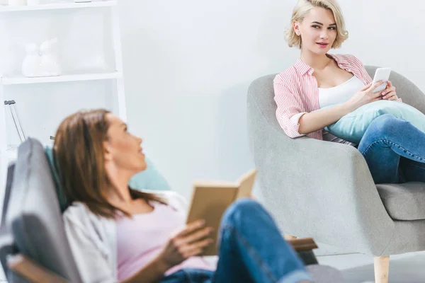 Amici Sesso Femminile Lettura Libro Utilizzando Smartphone Casa — Foto Stock