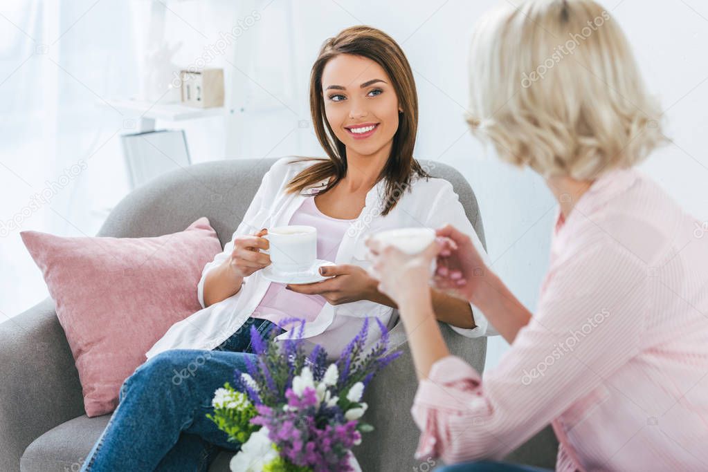 selective focus of girls with coffee cups talking and sitting on armchairs