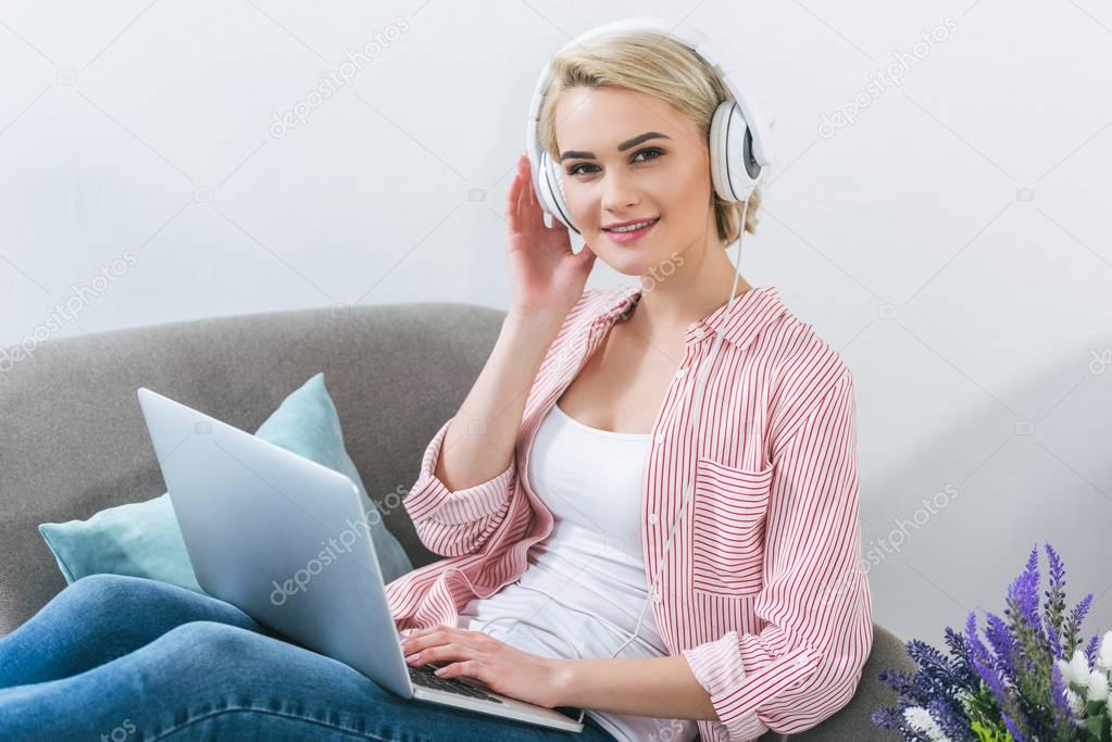 beautiful blonde girl listening music with headphones and using laptop