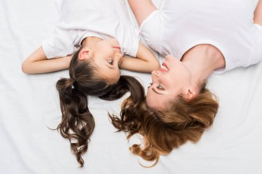 overhead view of mother and daughter looking at each other while lying on bed