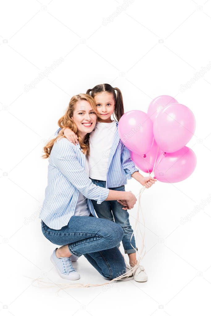 smiling mother and daughter with pink balloons hugging each other isolated on white