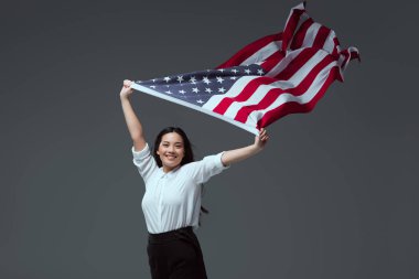 Amerikan bayrağı kaldırdı elinde tutan ve gri izole kamera gülümseyen güzel genç kadın