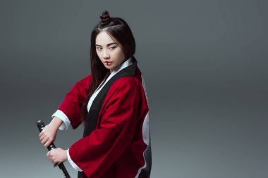 asian woman in kimono holding katana sword and looking away isolated on grey clipart
