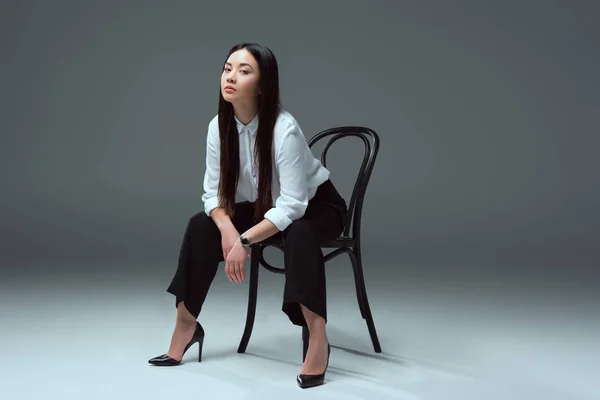 美しい若いアジア女性の椅子に座っているとグレーのカメラ目線のフルの長さの表示 — ストック写真