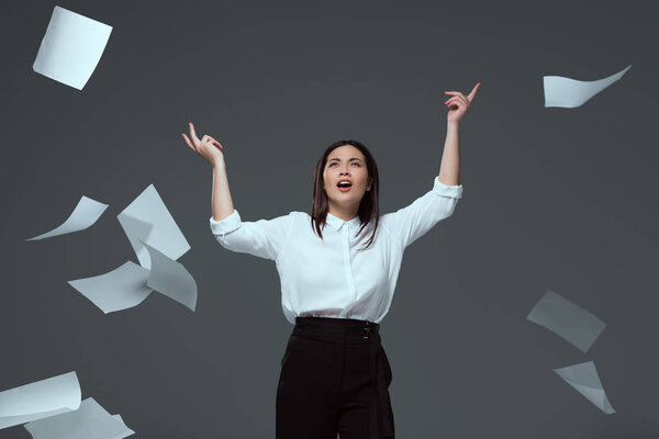 emotional young businesswoman throwing papers isolated on grey