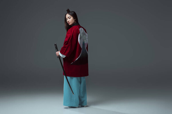 back view of samurai in kimono holding katana and looking at camera on grey  
