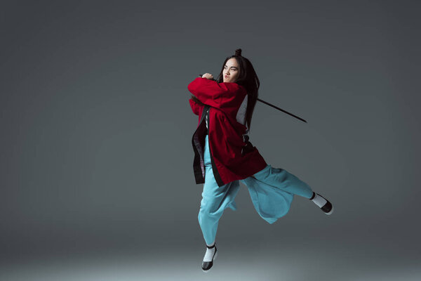 asian woman in kimono fighting with katana in jump on grey 