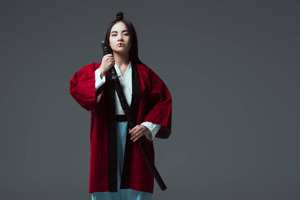 samurai in kimono holding katana sword and looking at camera isolated on grey