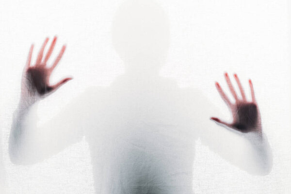 blurry silhouette of person touching frosted glass with hands
