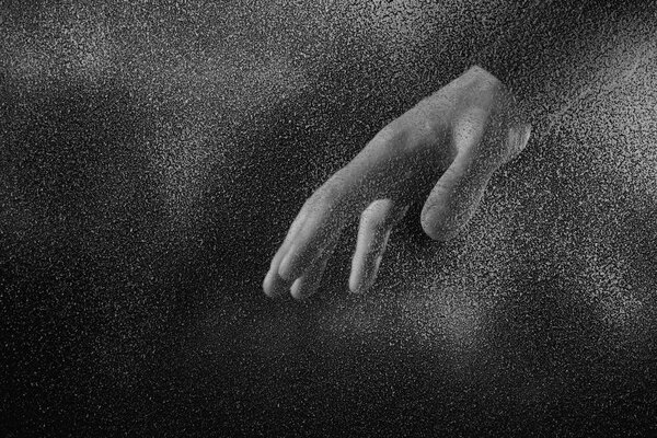 cropped shot of person showing hand through frosted glass in darkness 