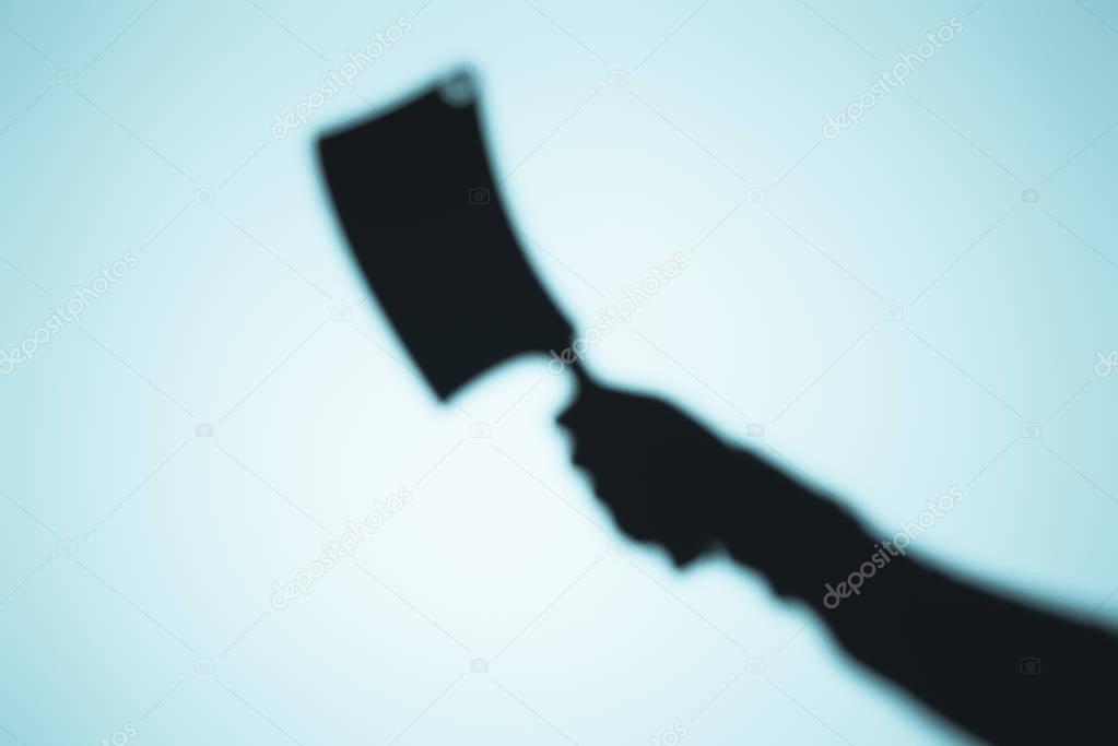 scary blurry shadow of person holding meat knife on blue