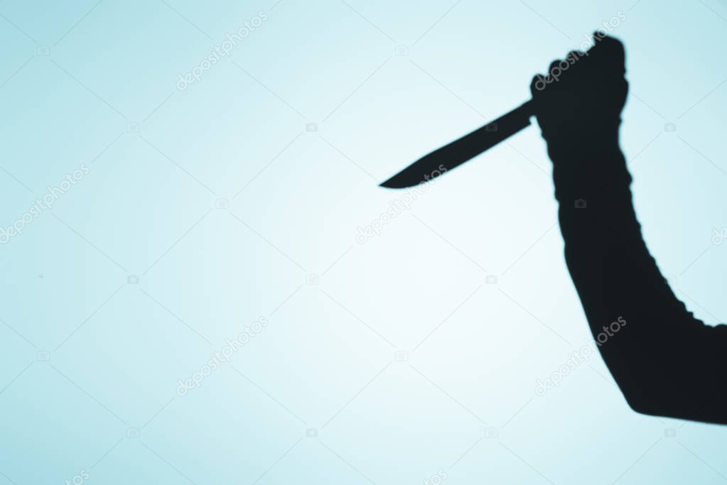 spooky shadow of person holding knife in hand on blue