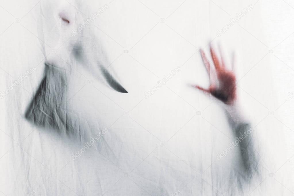 scary blurry silhouette of unrecognizable person holding knife behind veil