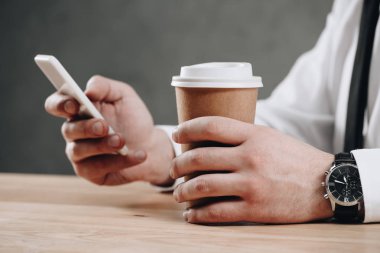 kağıt bardak tutan ve smartphone kullanarak işadamı kısmi görmek